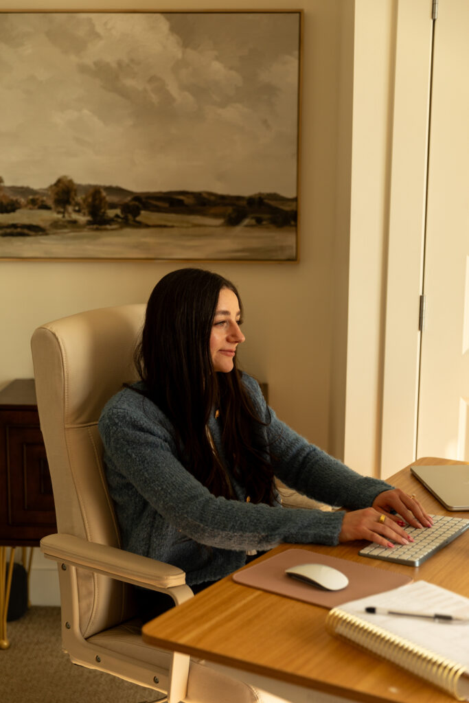 Abi of Flourish Foundry Designs sits at her computer to share a Showit vs Wix comparison on her website. 